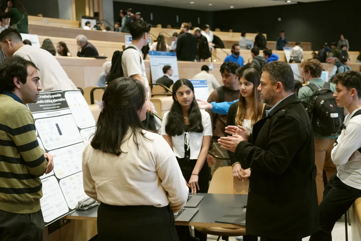 Mr. Aladdin Abujarad (second from right), from the team of administrators, speaks to students inside the Myhal Centre, where ECE’s 2024 Capstone Design Fair was held over three nights in April. (photo by Matthew Tierney)